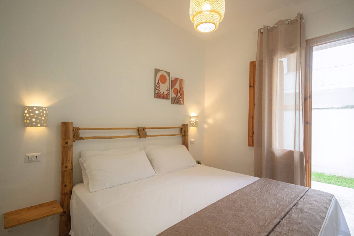 Ein Schlafzimmer mit einem hölzernen Bettgestell, weißer Bettwäsche, zwei Wandleuchten und einem Fenster mit Vorhängen.