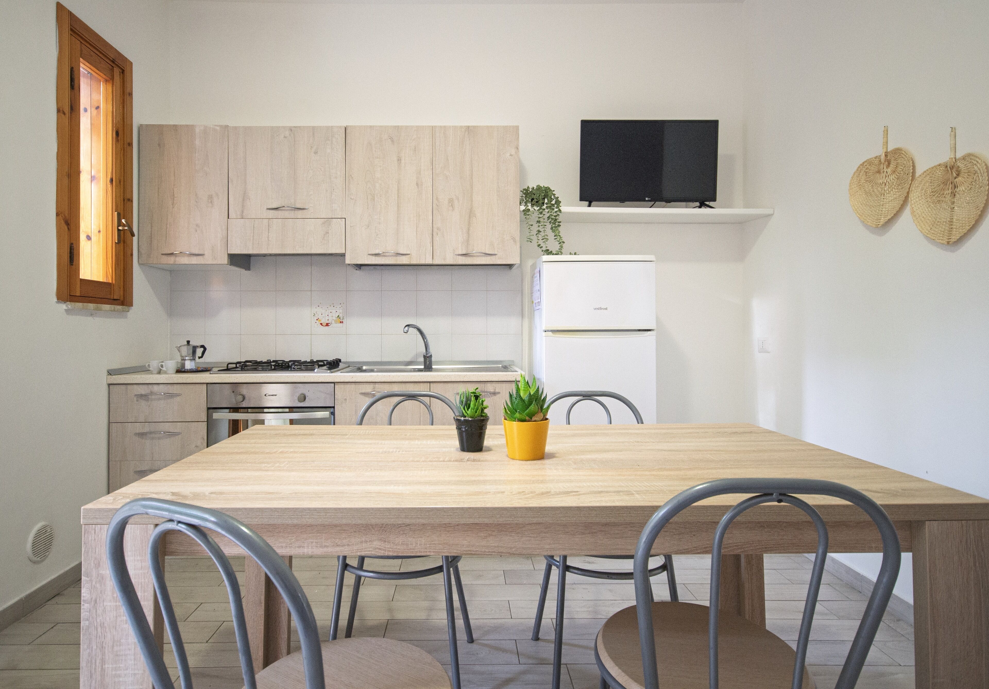 Una cocina moderna con armarios de madera, un refrigerador blanco, una mesa de comedor con sillas y un televisor sobre la encimera.