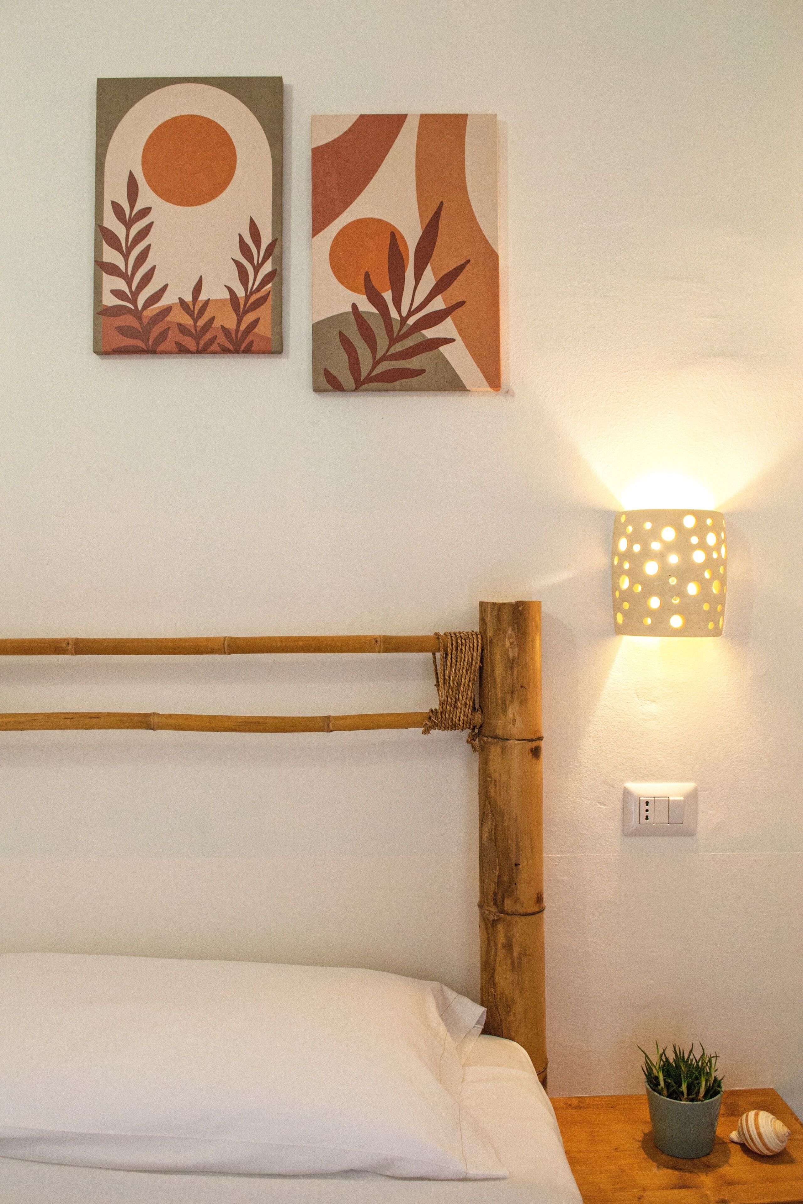 A bedroom with a wooden headboard, a bedside lamp, a small plant, and two wall art pieces.