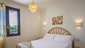 Een slaapkamer met een bed, een raam, een wandlamp en een kunstwerk aan de muur.