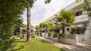 Een verzorgde tuin met een wit gebouw, palmbomen en een pergola.