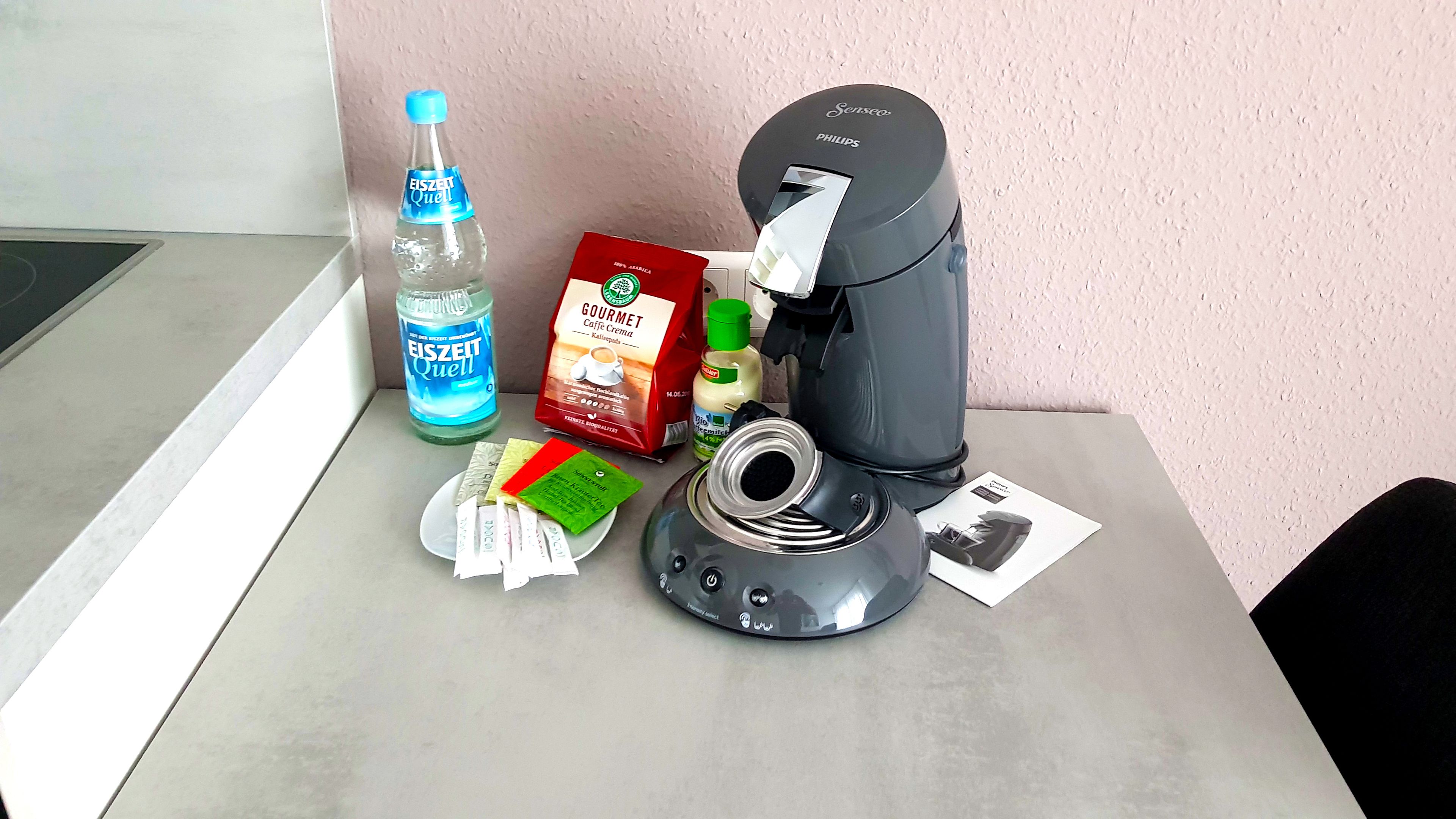 Una macchina da caffè, una bottiglia d'acqua, una confezione di crema per caffè e cialde di caffè su un tavolo.