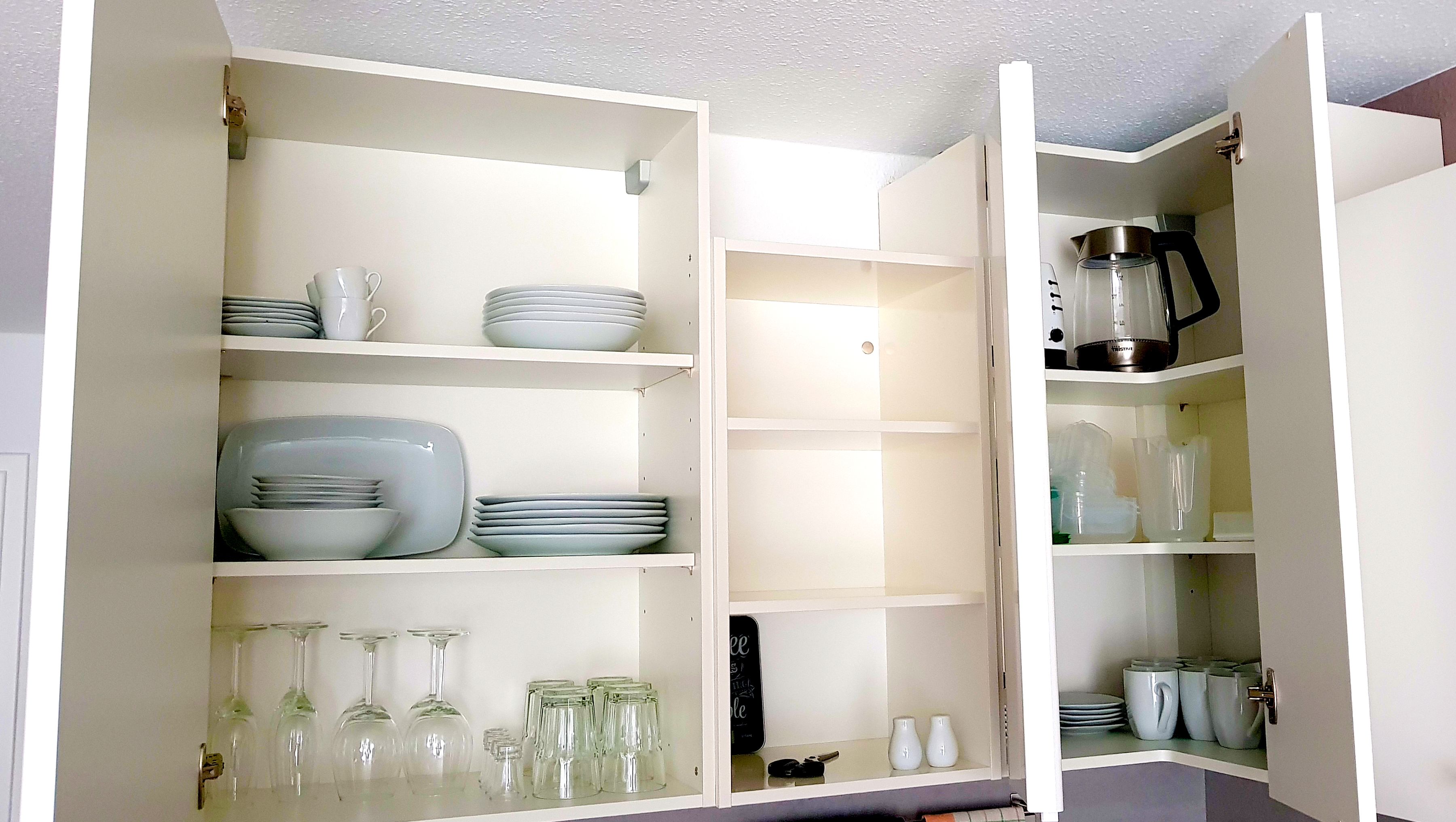 A kitchen with open cabinets displaying dishes, glasses, and a coffee maker.