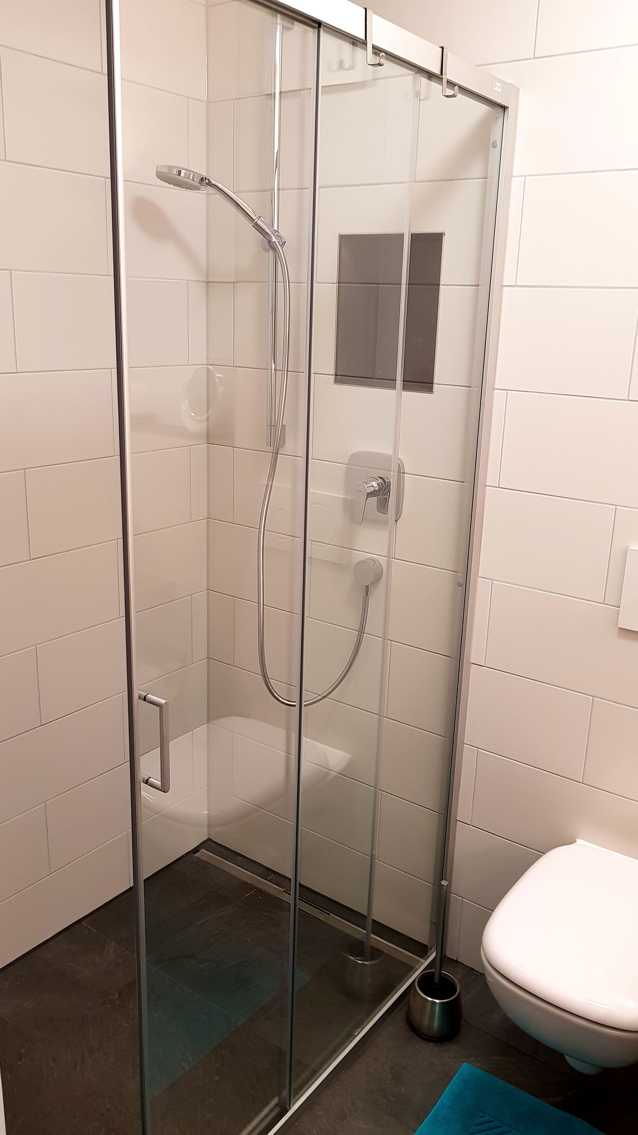 A glass-enclosed shower stall with a handheld showerhead and a wall-mounted faucet.