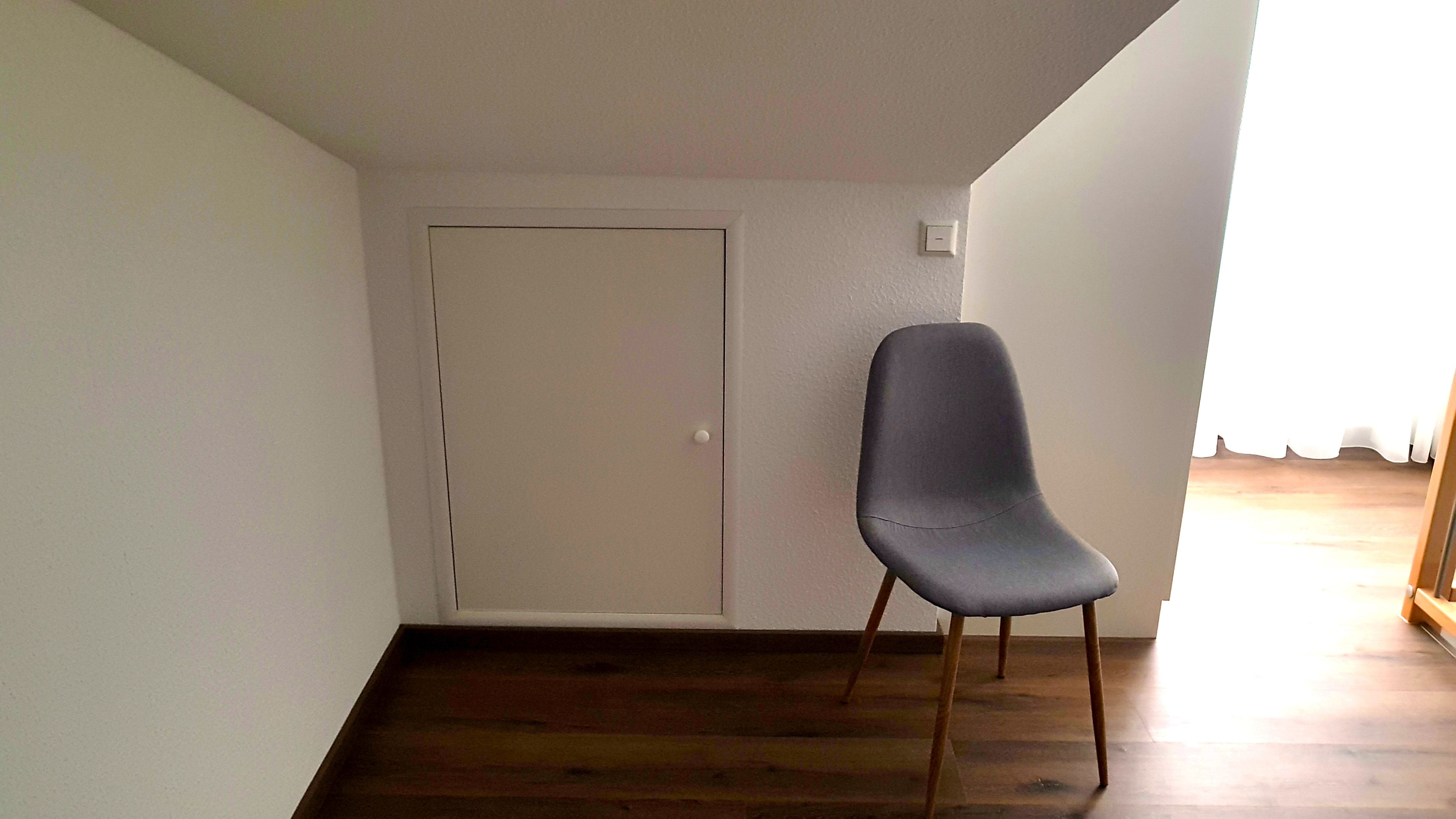 Una habitación con piso de madera, una puerta blanca y una silla gris.