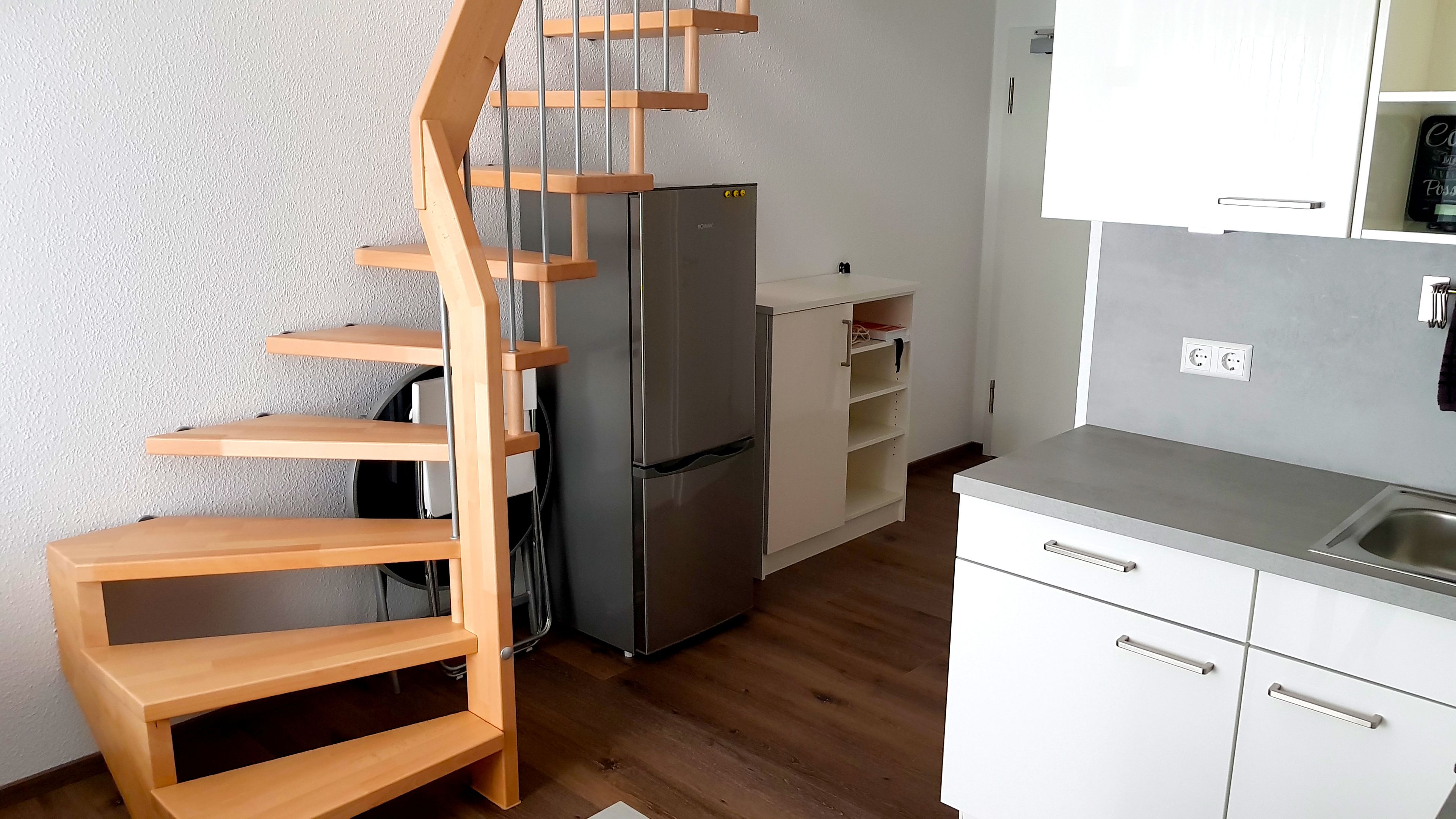 A compact kitchen with a built-in refrigerator, wooden staircase, and white cabinetry.