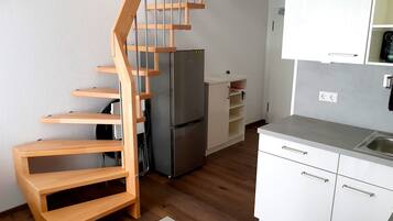 A compact kitchen with a built-in refrigerator, wooden staircase, and white cabinetry.