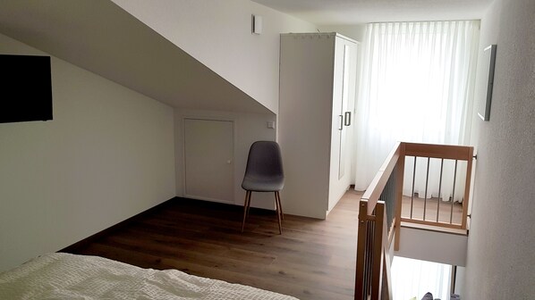 A bedroom with a bed, a chair, a wardrobe, and a staircase. - Neckarzeit (Neckarwestheim)