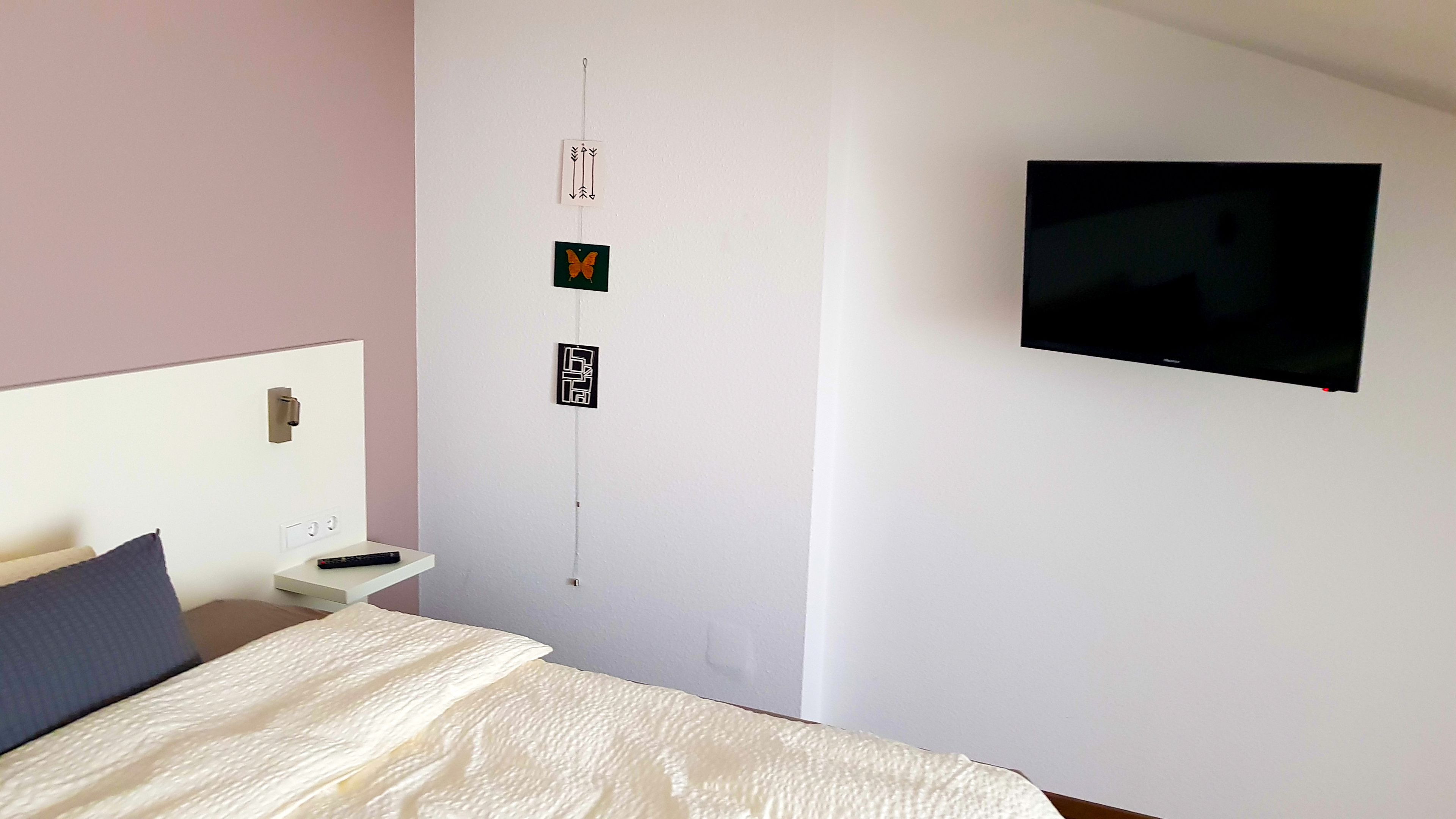 Une chambre à coucher comprenant un lit, une table de chevet, un téléviseur fixé au mur et un mur orné de trois éléments décoratifs.
