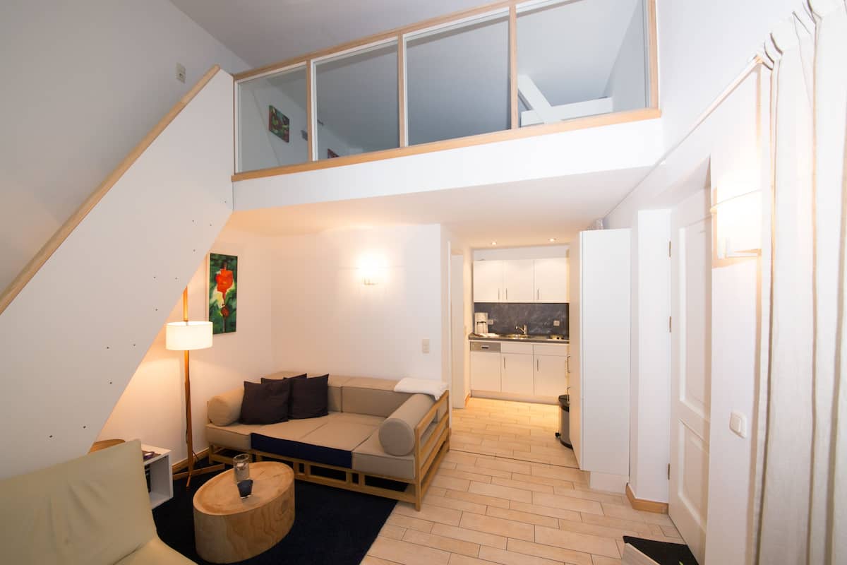 A modern loft apartment with a loft bed, a sofa, a dining area, and a kitchen.
