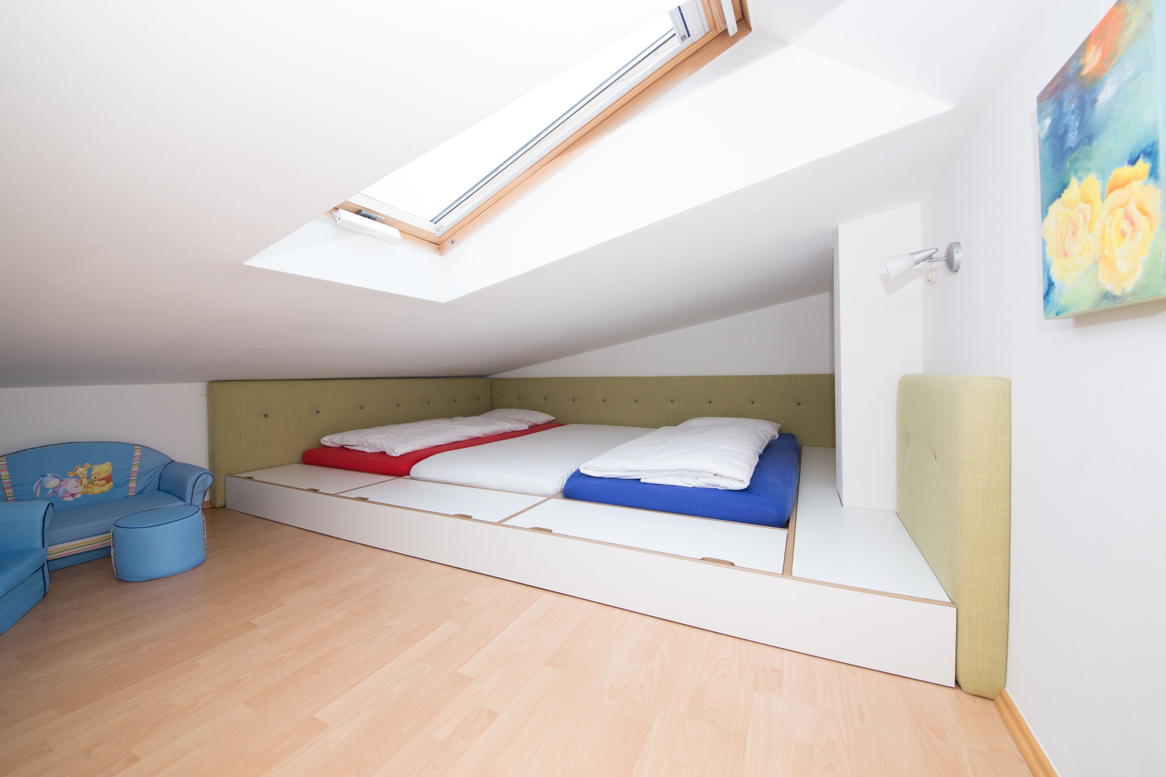 A bedroom with a skylight, a bed with blue and red bedding, a blue sofa, and a small ottoman.