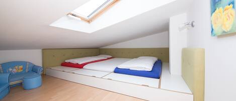 A bedroom with a skylight, a bed with blue and red bedding, a blue sofa, and a small ottoman.
