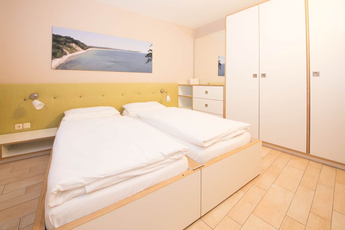 A bedroom with a bed, a nightstand, a wardrobe, and a painting of a beach scene.