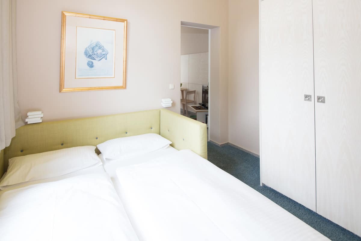 A hotel room with a double bed, a framed picture on the wall, a wardrobe, and a mirror reflecting a bathroom.