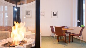 Un salon moderne avec une cheminée en verre, un coin repas avec une table ronde et des chaises, et des tableaux encadrés accrochés au mur.