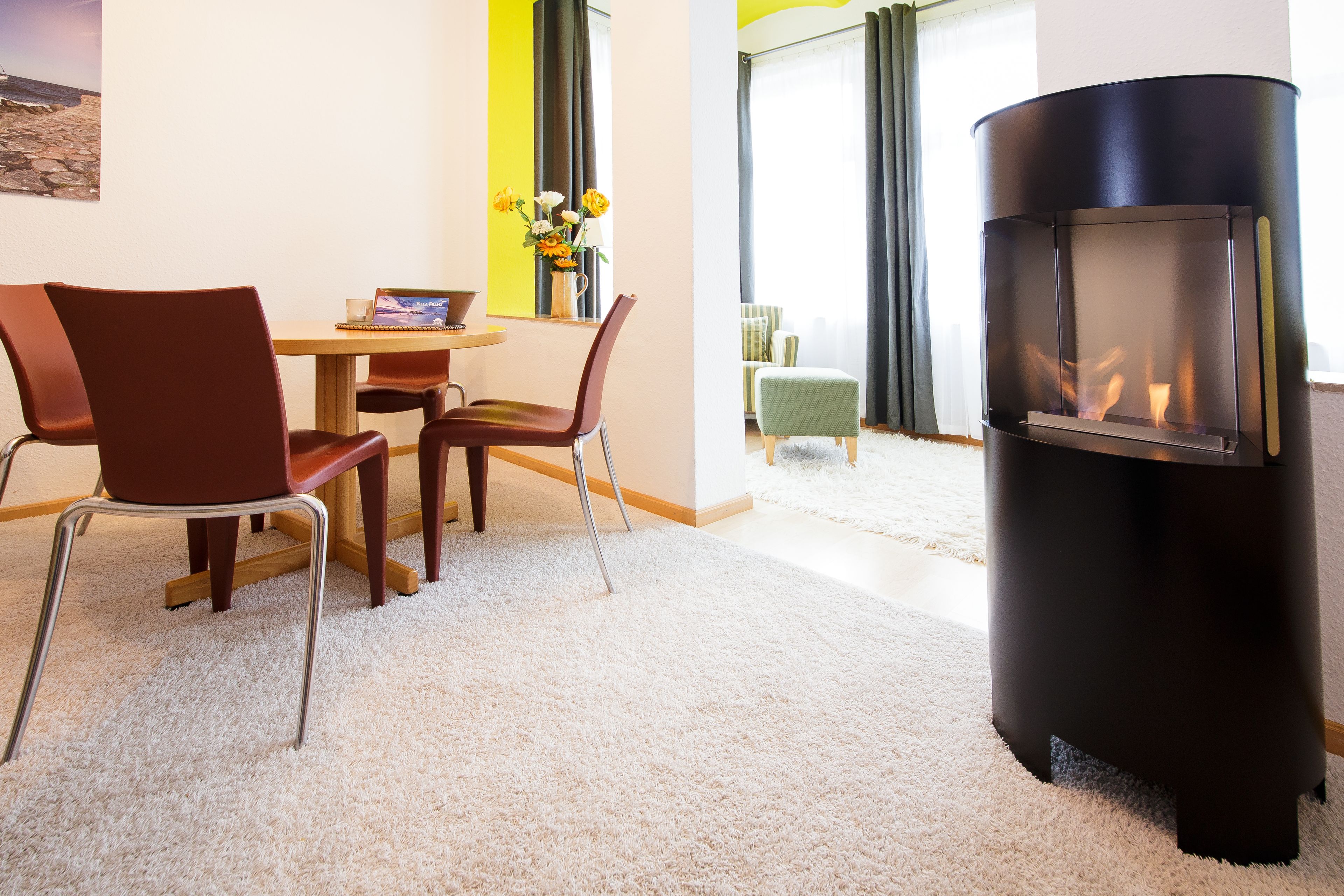 Een moderne woonkamer met een open haard, een eethoek met een tafel en stoelen, en uitzicht op de omgeving door grote ramen.