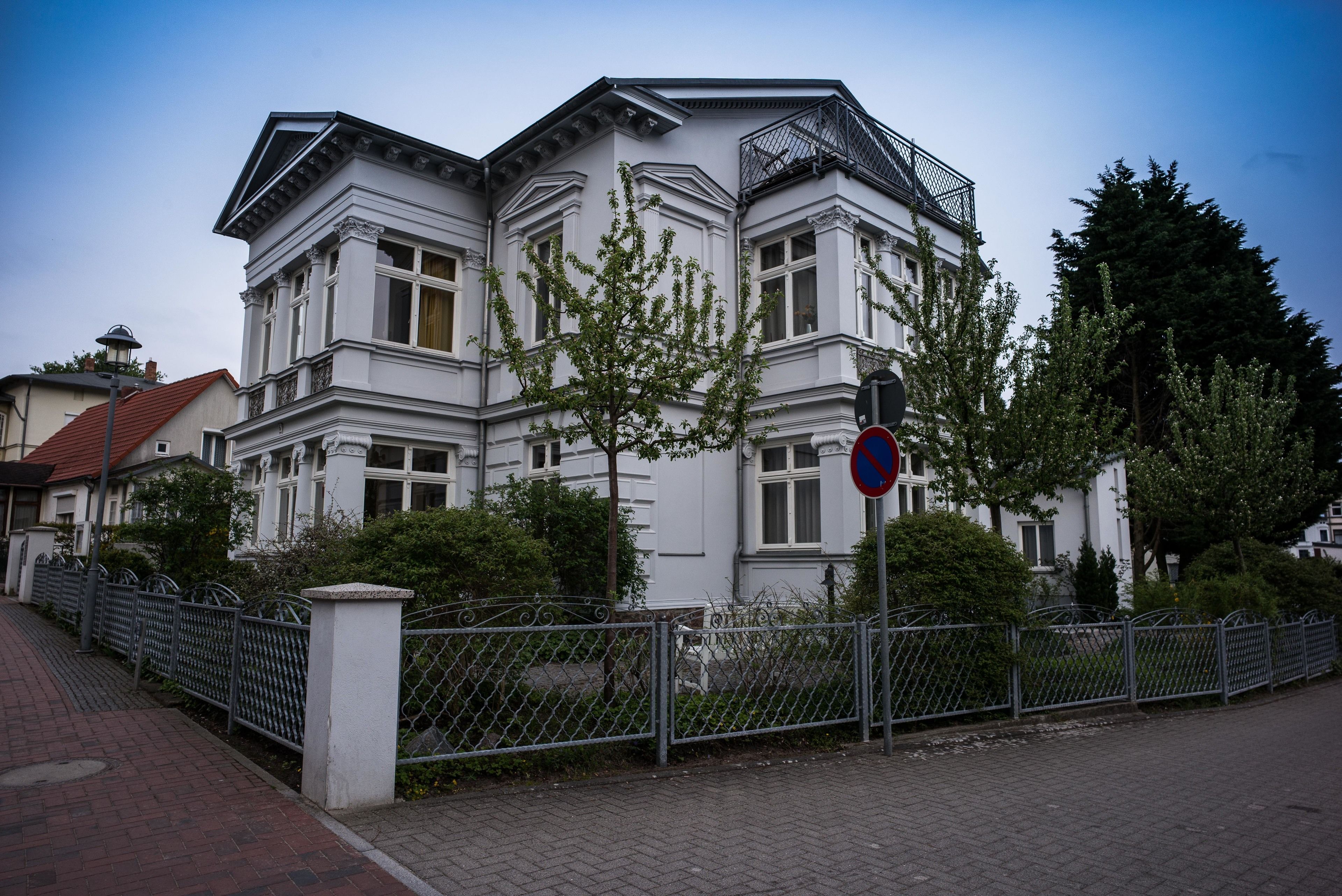 Un bâtiment blanc avec une entrée située à l’angle, une clôture en métal et un panneau indiquant qu’il est interdit de se garer.