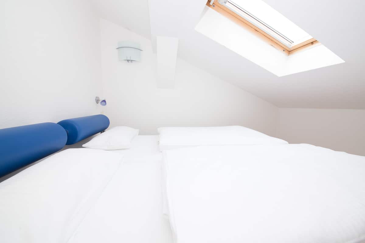 A bedroom with a skylight, a bed with white bedding, and a blue headboard.