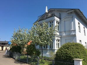 A white building with a balcony, surrounded by trees and a metal fence. - Villa Franz (Heringsdorf)