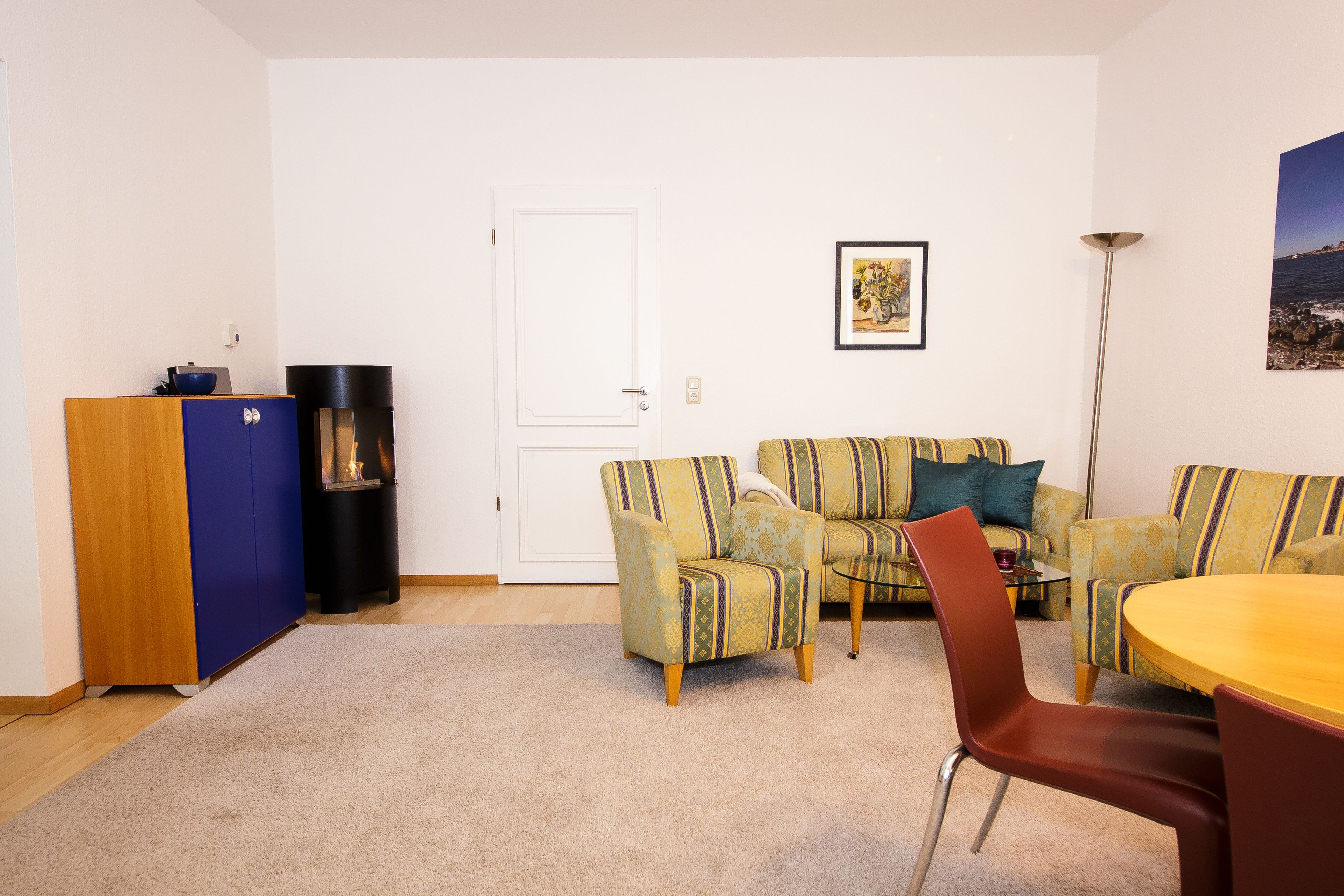 A living room with a sofa, chairs, a coffee table, a cabinet, and a door.