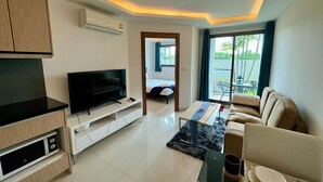 A modern living room with a flat-screen TV, a sofa, a coffee table, and a dining area with a table and chairs. - Maldives Resort by PSR ASIA (Pattaya)