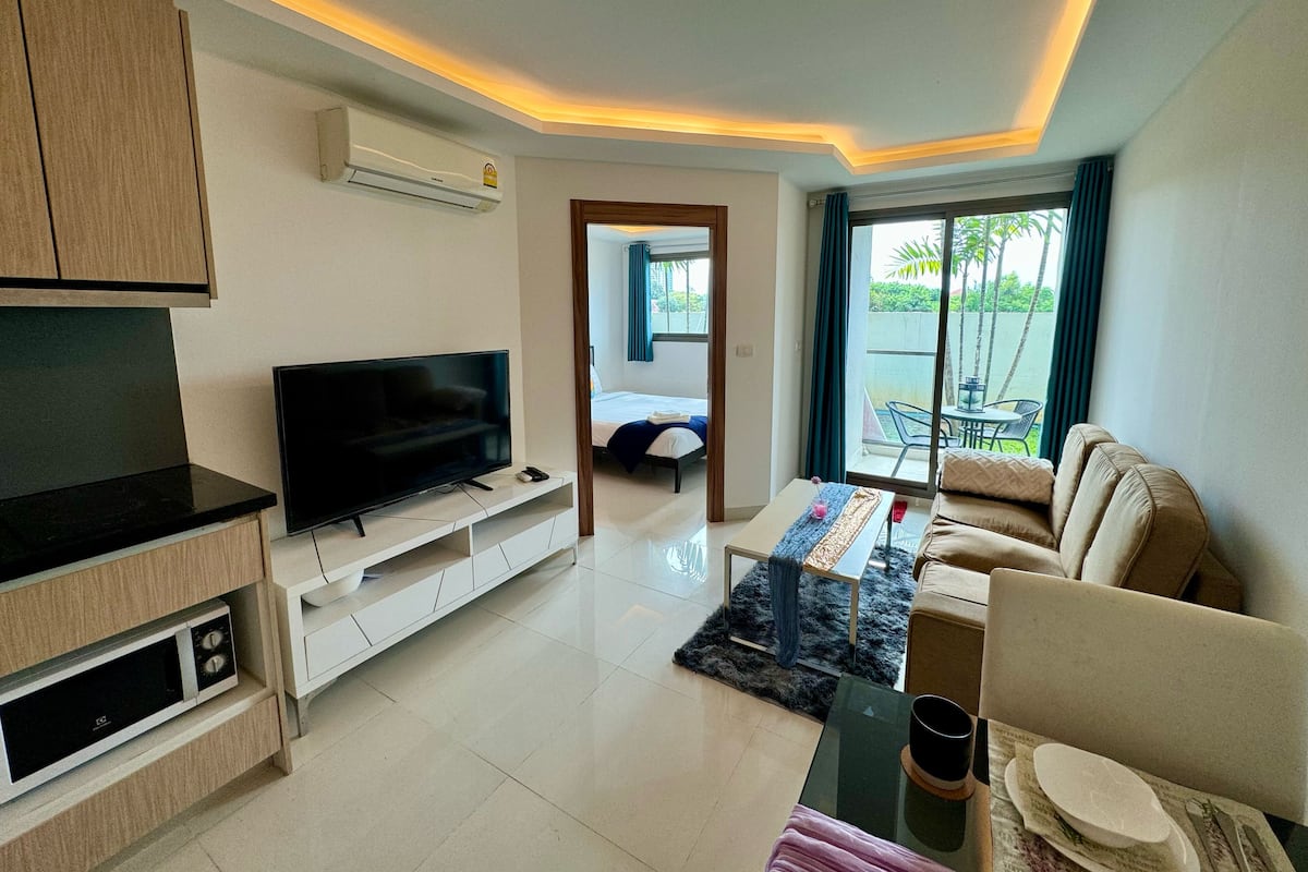 A modern living room with a flat-screen TV, a sofa, a coffee table, and a dining area with a table and chairs.