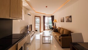 A modern hotel room with a kitchenette, a sofa, a dining table, and a view of the city. - Maldives Resort by PSR ASIA (Pattaya)