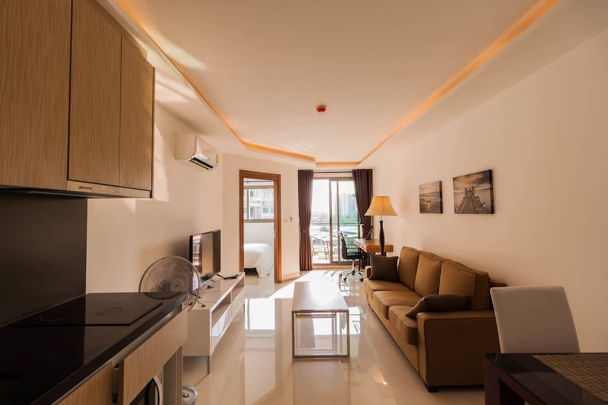 A modern hotel room with a kitchenette, a sofa, a dining table, and a view of the city.
