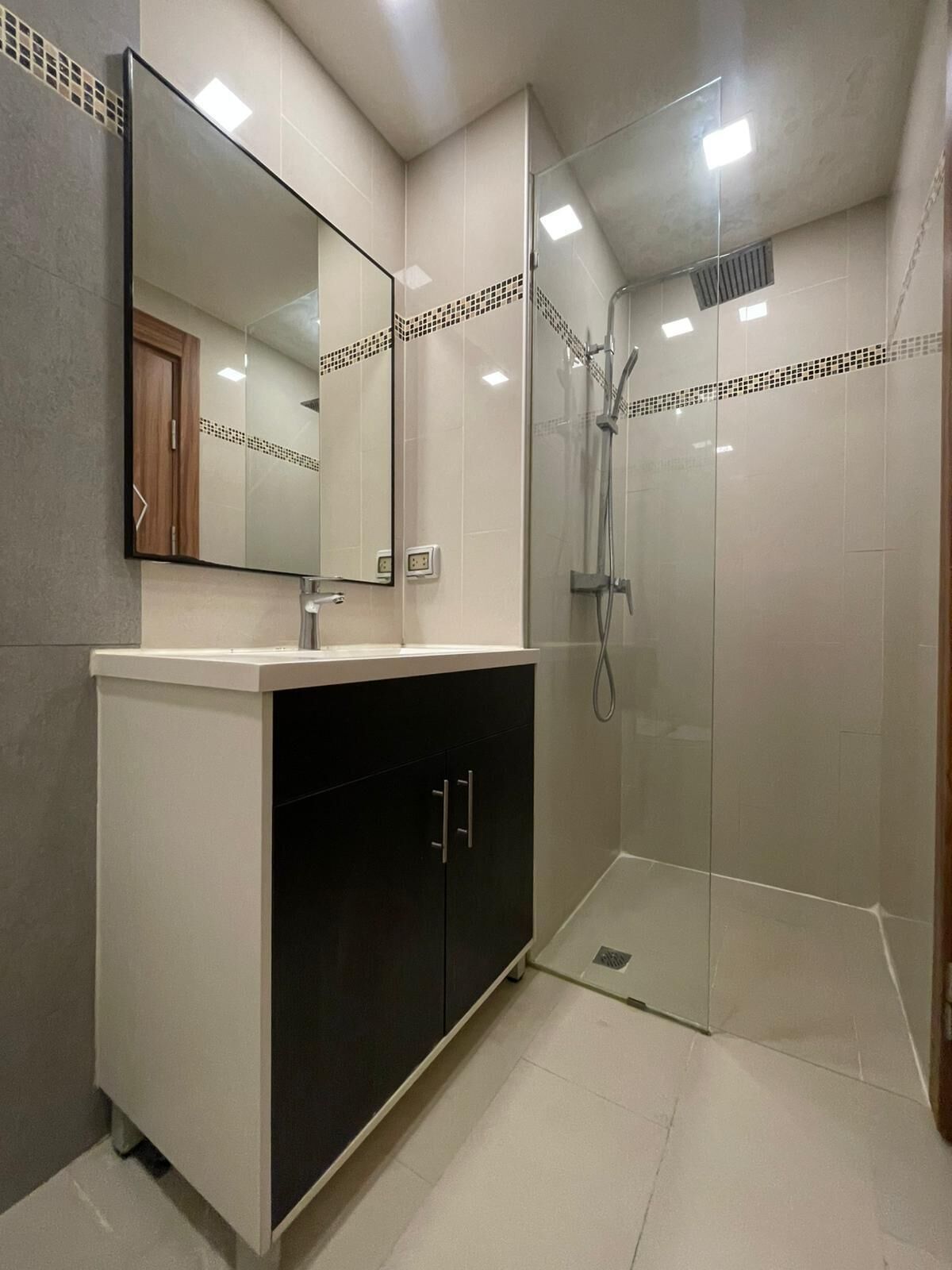 A modern bathroom with a glass shower enclosure, a large mirror, and a dark-toned cabinet.