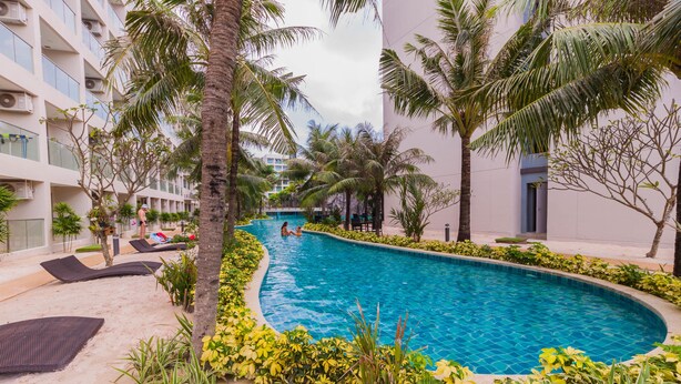 A swimming pool surrounded by palm trees and lounge chairs, with a building in the background. - Maldives Resort by PSR ASIA (Pattaya)
