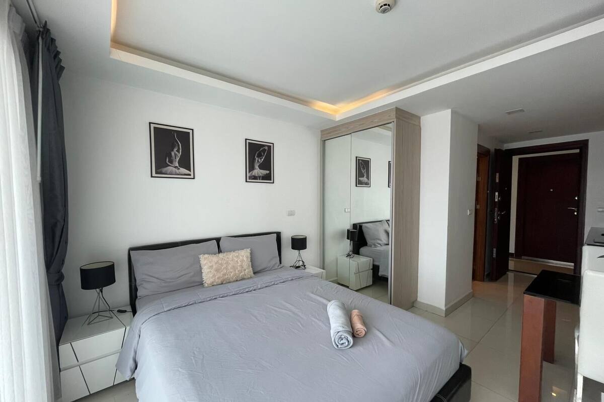A modern hotel room with a large bed, bedside tables, a mirror, and a desk.