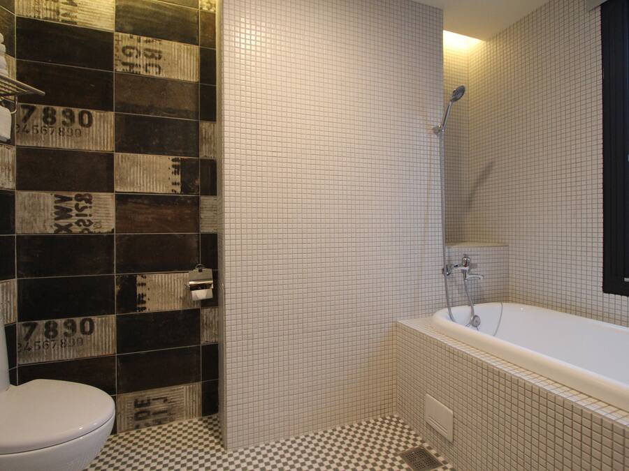 Une salle de bain avec un carrelage à motifs géométriques, des toilettes, une baignoire et des murs recouverts de carreaux ornés de chiffres.