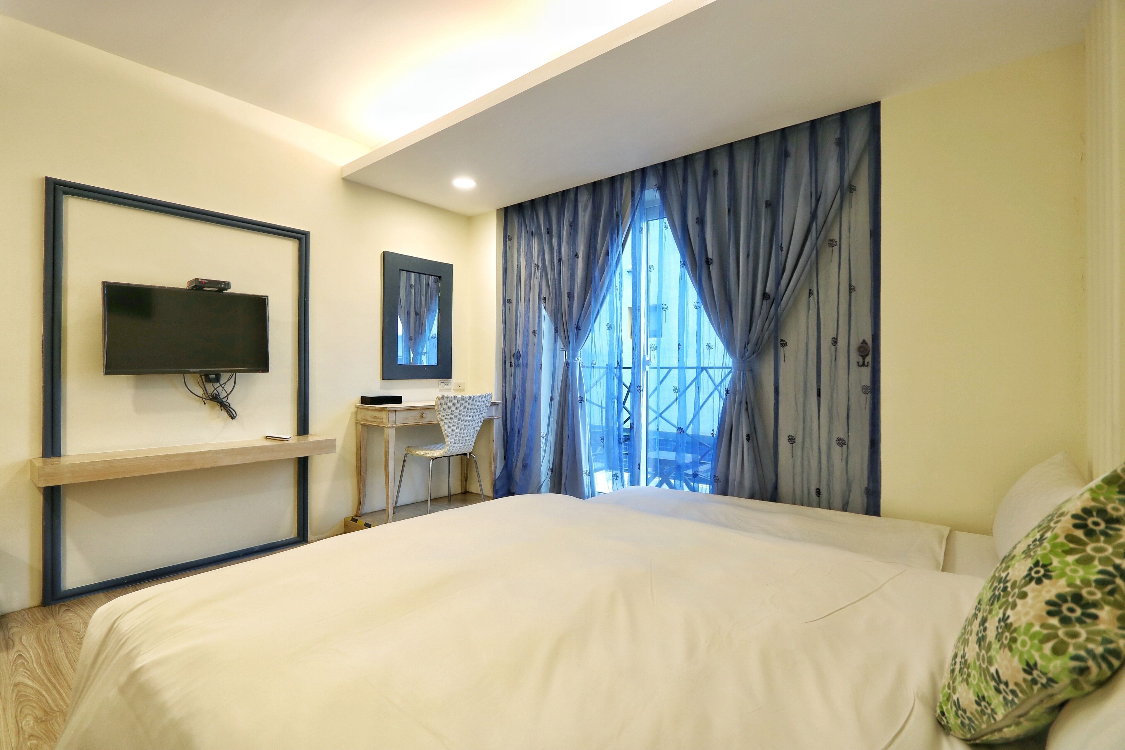 A hotel room with a large bed, a desk with a chair, a television mounted on the wall, and a window with curtains.