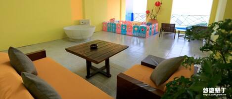 Una habitación con sofás naranjas, una mesa de centro de madera, una bañera blanca y cajas de almacenamiento de colores.