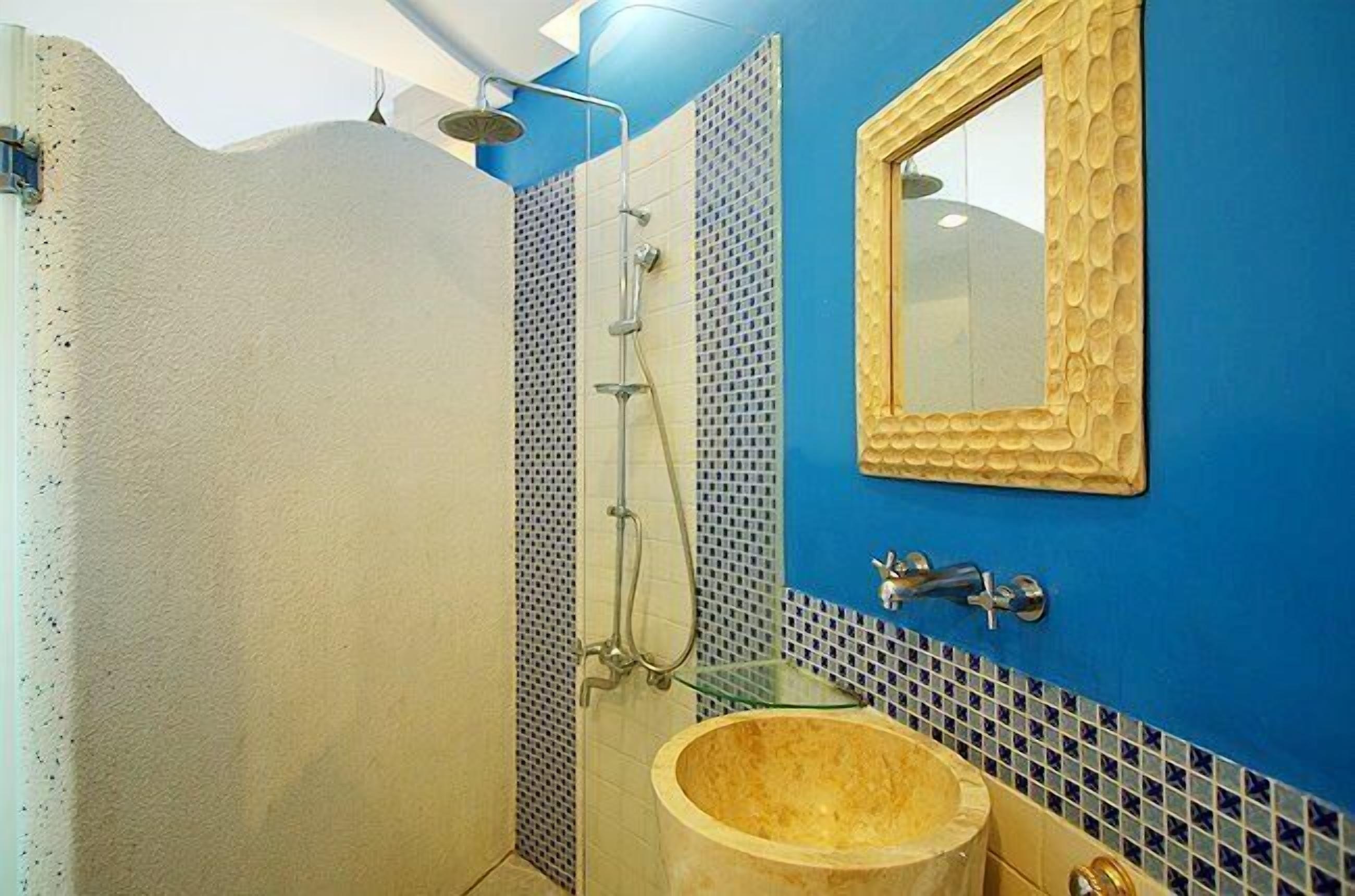 A bathroom with a shower, a sink with a wooden basin, and a mirror with a decorative frame.