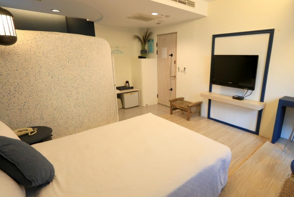A modern hotel room with a large bed, a desk, a TV, and a small seating area.
