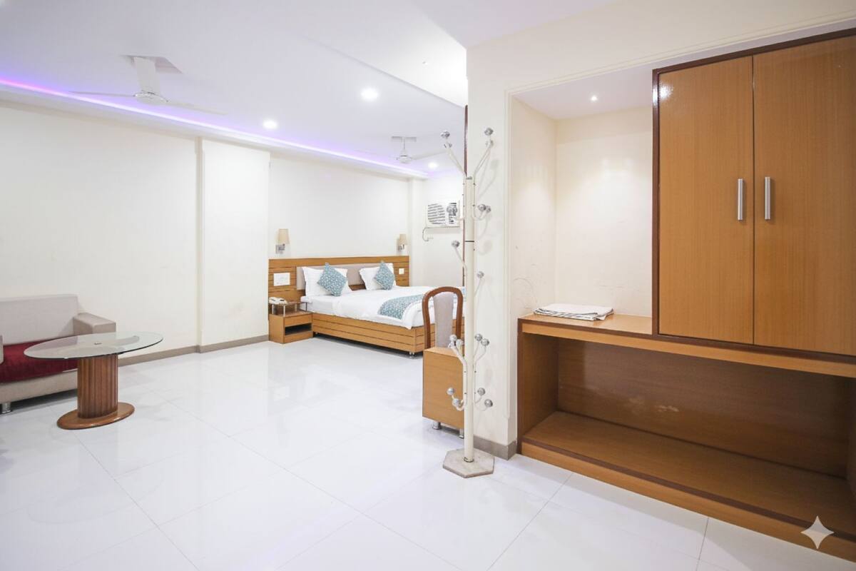A modern hotel room with a bed, a desk, a wardrobe, and a seating area.