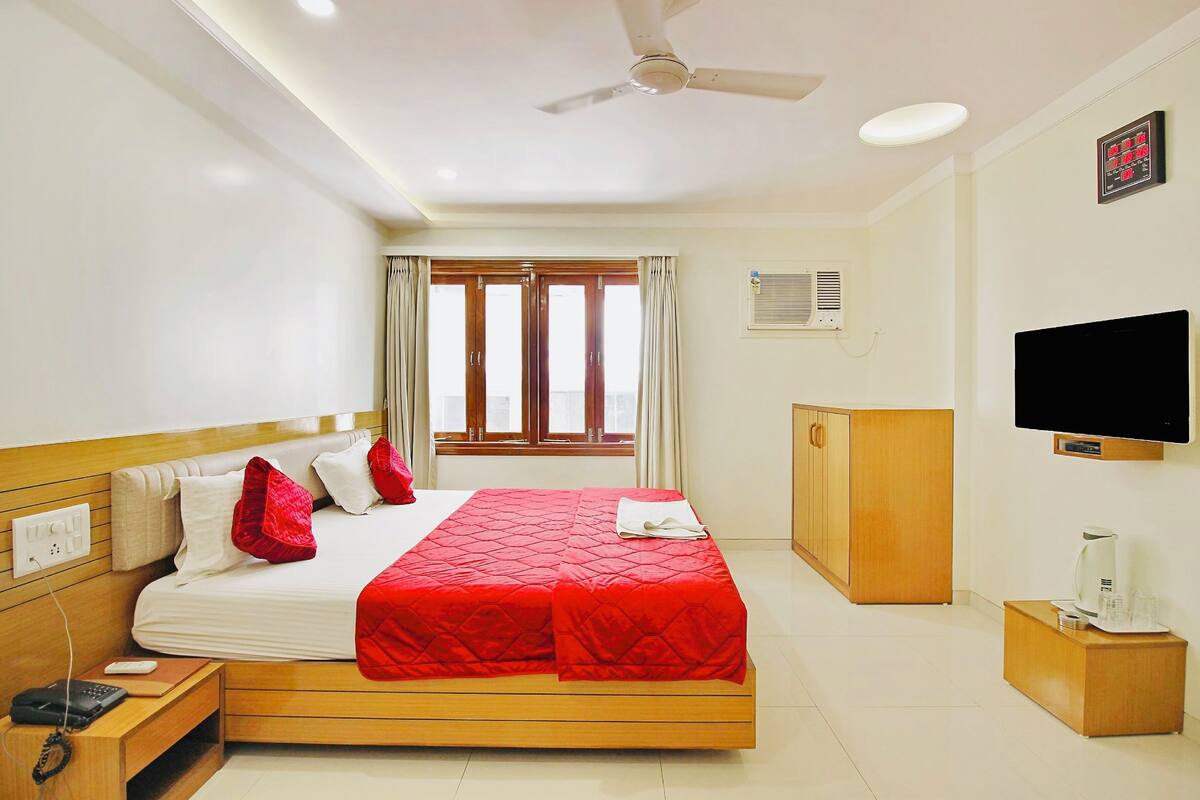 A hotel room with a bed, wooden headboard, a television, a desk with a telephone, and a window with curtains.