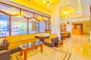 A hotel lobby with a yellow sofa, a glass coffee table, and a reception desk. - Hotel Sarita (Surat)