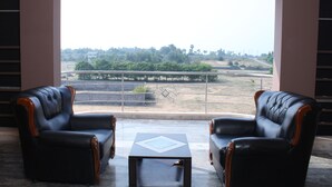 Una habitación con dos sillones de cuero negro y una pequeña mesa cuadrada, un ventanal con vistas a un paisaje verde y edificios a lo lejos.