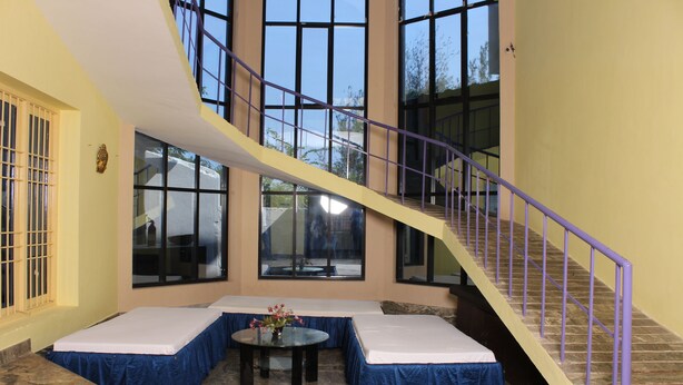 Una habitación con una escalera curva, ventanas amplias, una mesa redonda con un florero y dos camas con ropa de cama azul.