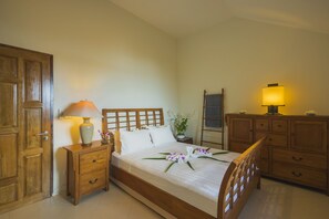 Una cama bien hecha con cabecera de madera, una mesita de noche con lámpara, un aparador y una puerta.