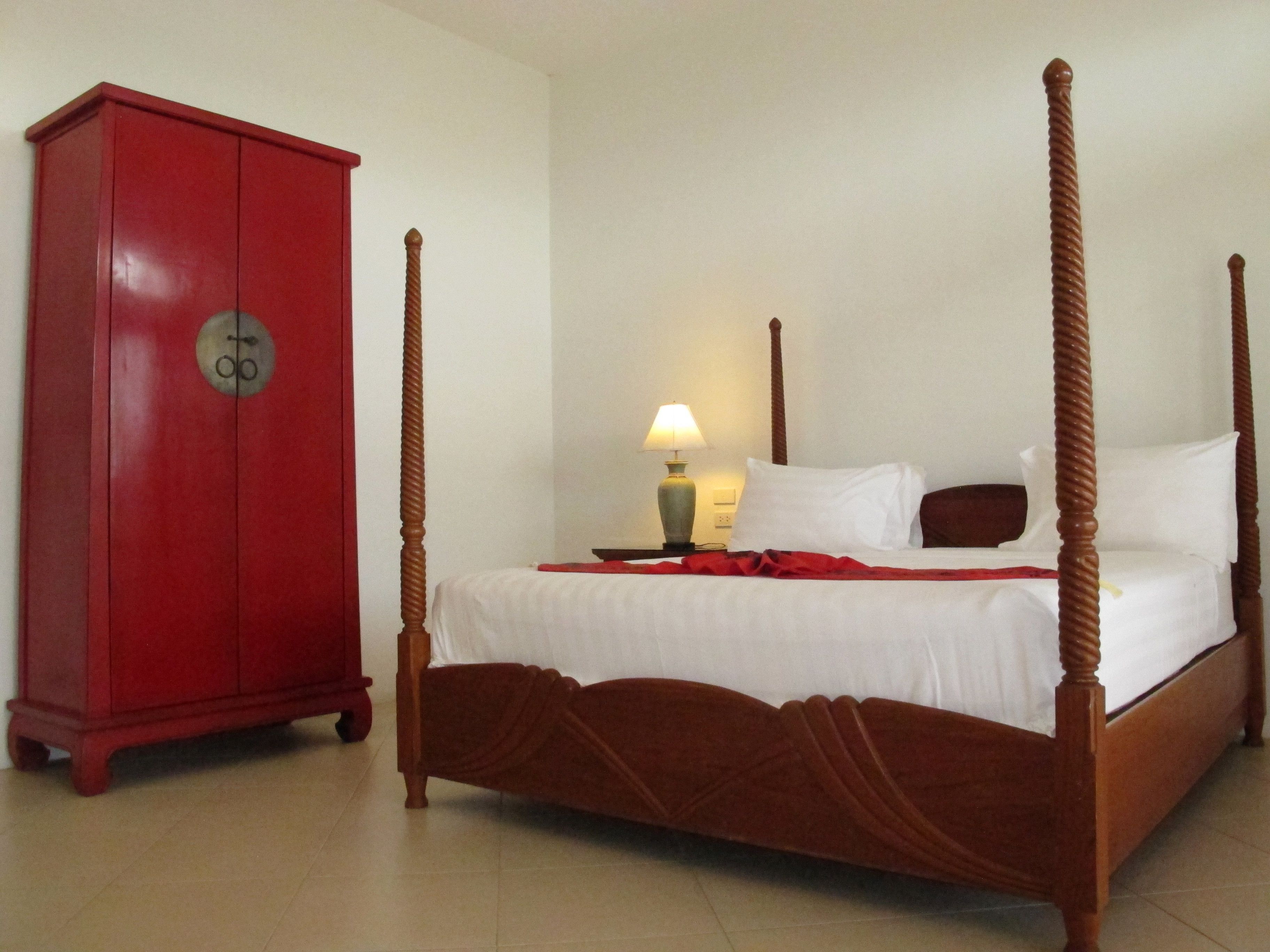 A four-poster bed with white linens, a red cabinet, and a bedside lamp.
