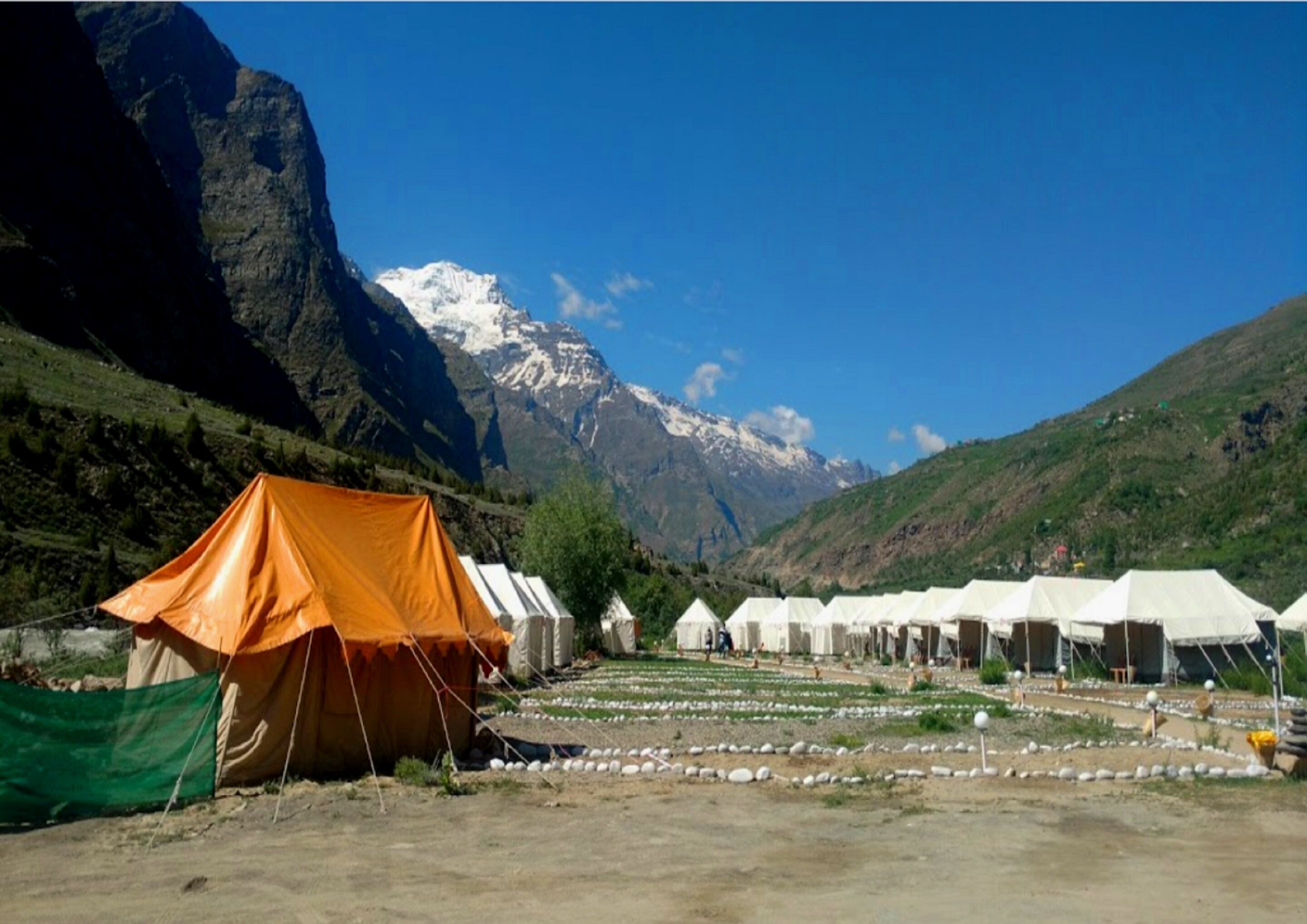 A row of tents in a mountainous area with a snow-capped peak in the background.