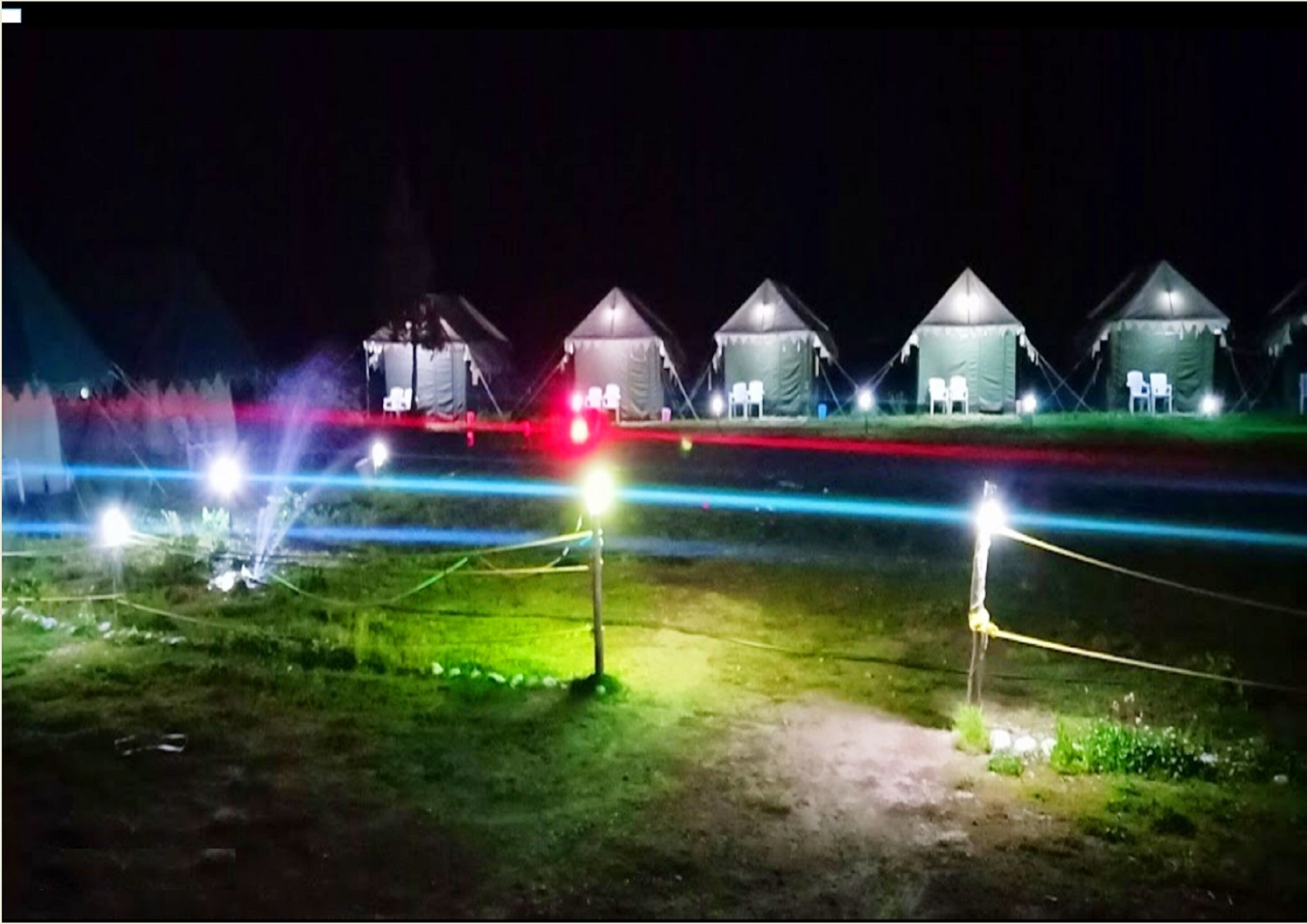 A row of tents with attached lights, surrounded by a grassy area with ropes.