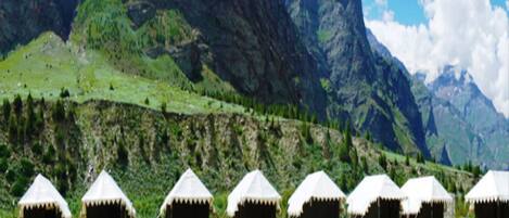 A row of white tents with thatched roofs, set against a mountainous backdrop.