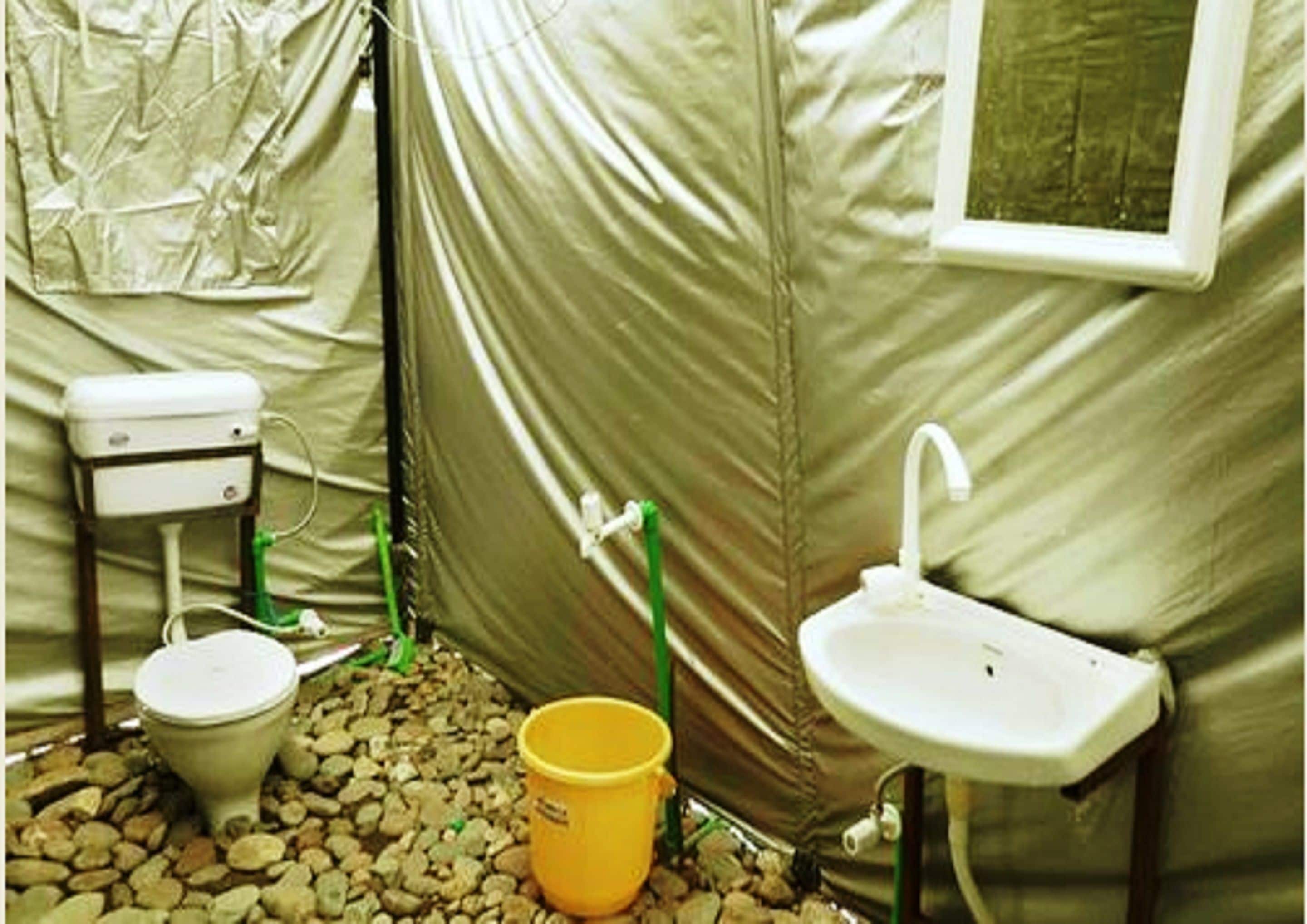 A compact, enclosed bathroom with a toilet, sink, and a small yellow bucket.