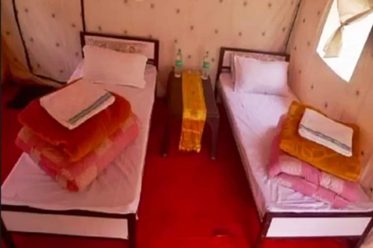 A room with two beds, each with a pillow and a folded blanket. There are two bottles on a small table between the beds.