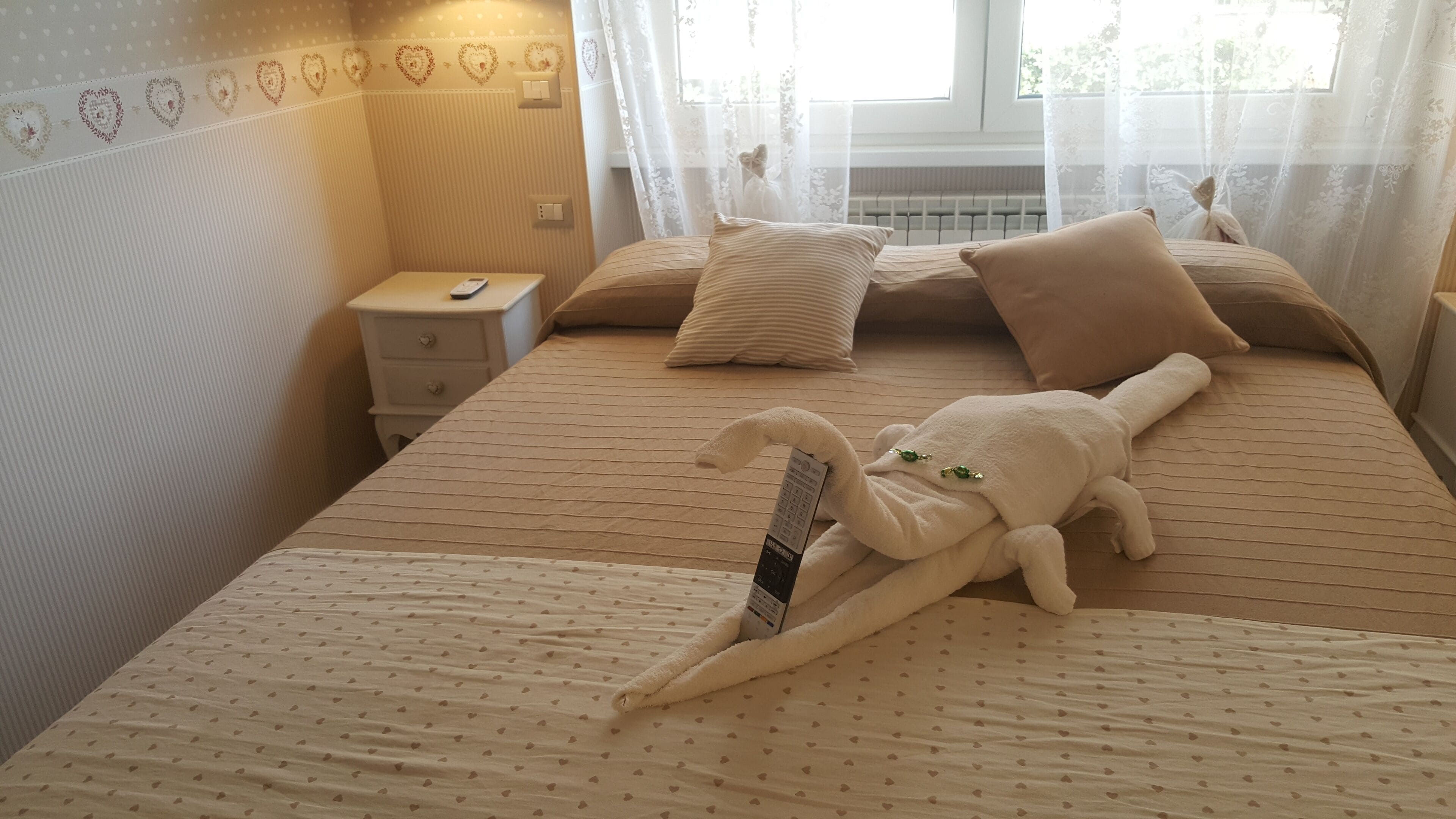 A hotel room with a bed, pillows, a nightstand, and a remote control.