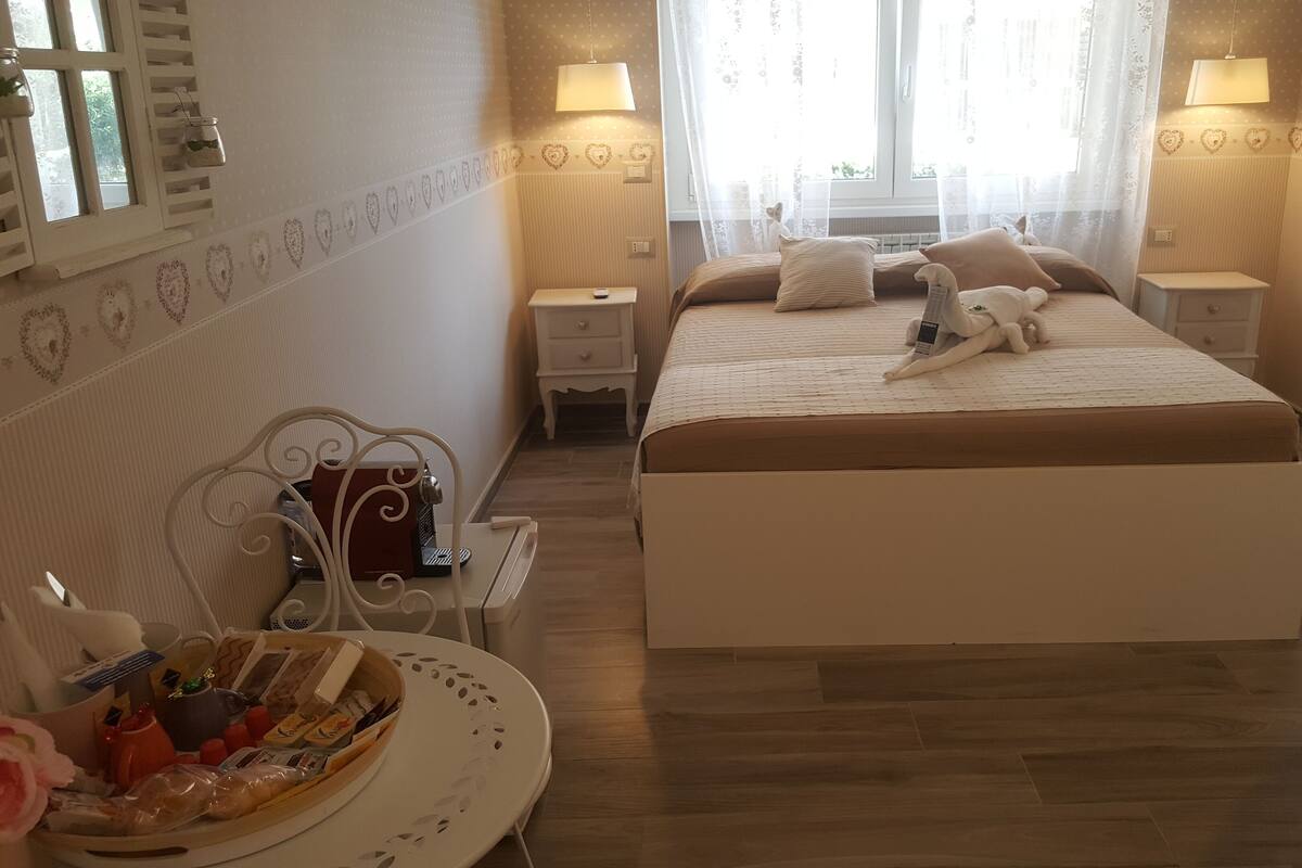 Un dormitorio con cama, mesitas de noche, una silla y una pequeña mesa con una cesta.